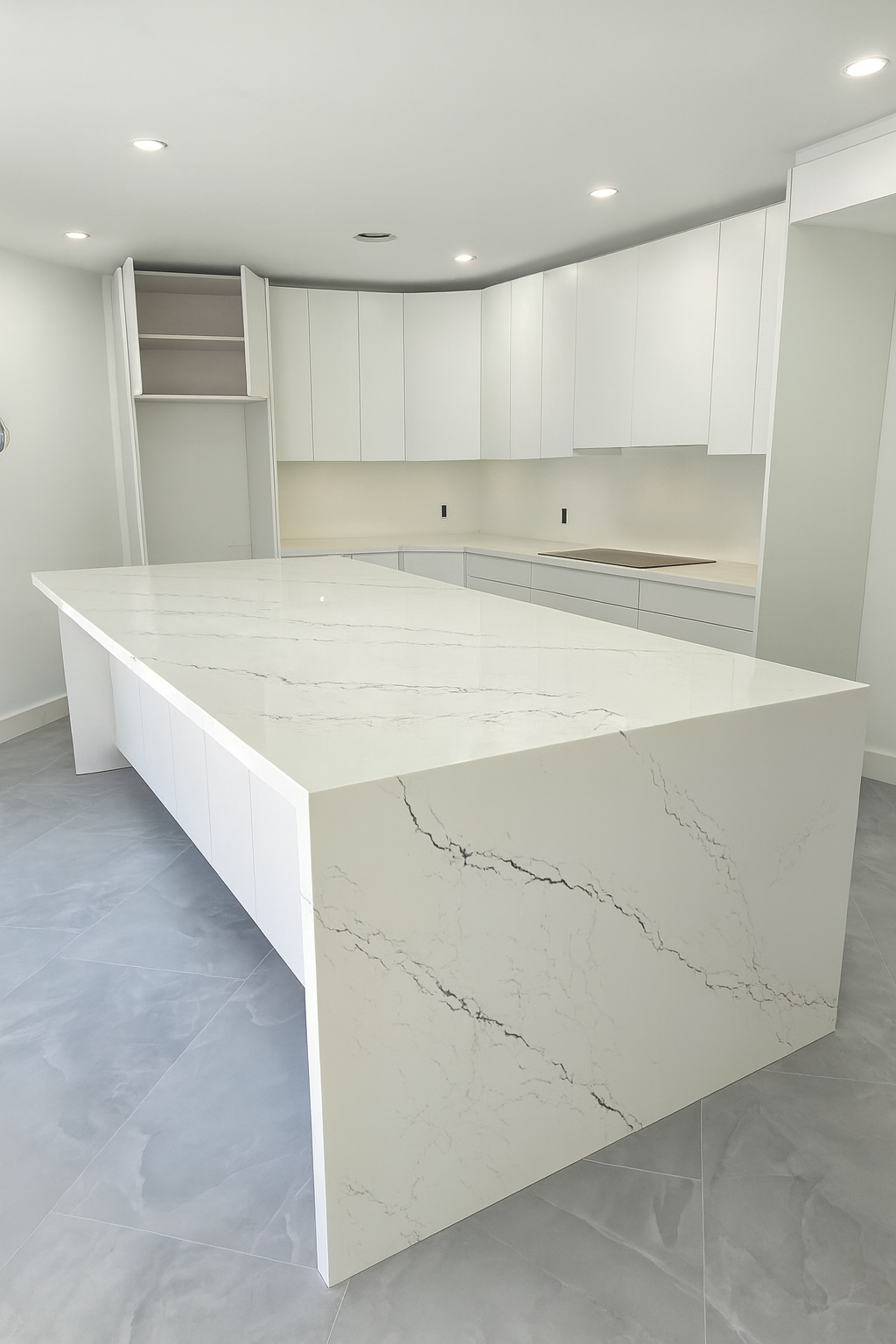 Contemporary kitchen featuring a large white quartz waterfall island with subtle gray veining, sleek white cabinetry, under-cabinet lighting, and polished gray tile flooring for a clean and modern design.