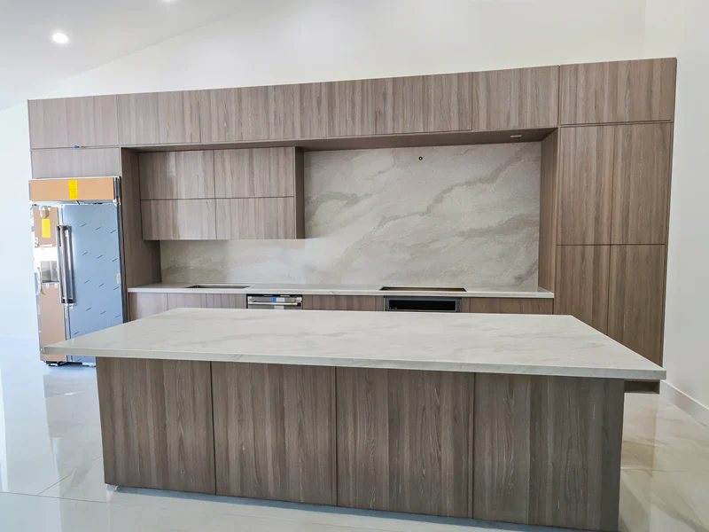 Newly installed cream quartz island and full-height backsplash on gray wood-grain cabinets